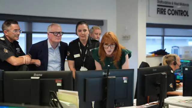 Angela Rayner, wearing a green dress, leans over to look at a computer screen while visiting a fire control room.