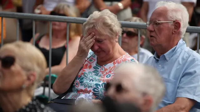 A woman places a hand on her head, crying.