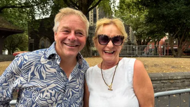 A man and a woman are stood next to each other, smiling