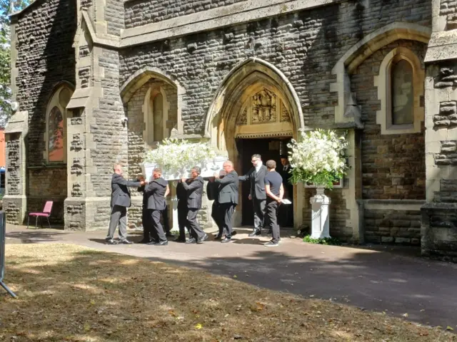 pallbearers carry a casket in front of a stone church
