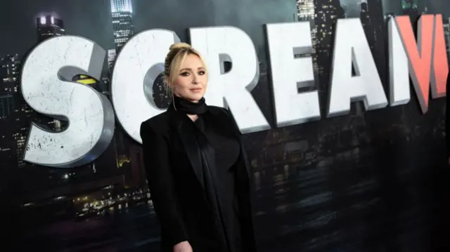 Panettiere stands in front of Scream VI poster in black blazer on red carpet