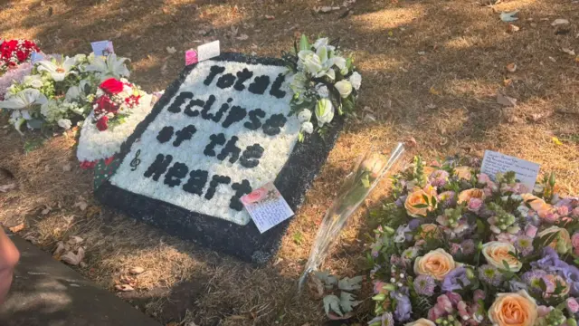 Floral tributes are laid on the floor , including one which says Total Eclipse of the Heart