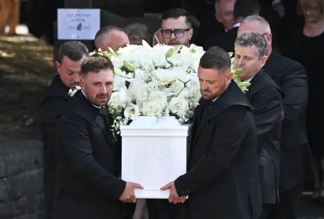 Male pale bearers carry a white coffin