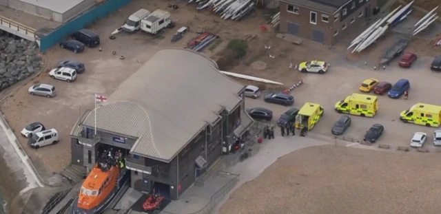 Lifeboat half in and half out of storage shed, three ambulances are behind it.