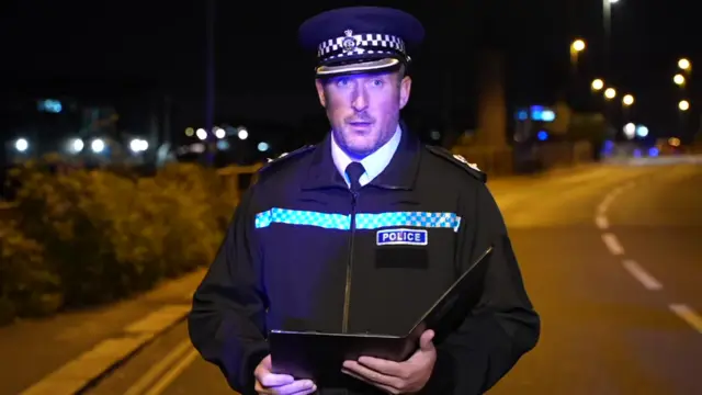 A police officer reads a written statement on a dark road by the ocean.