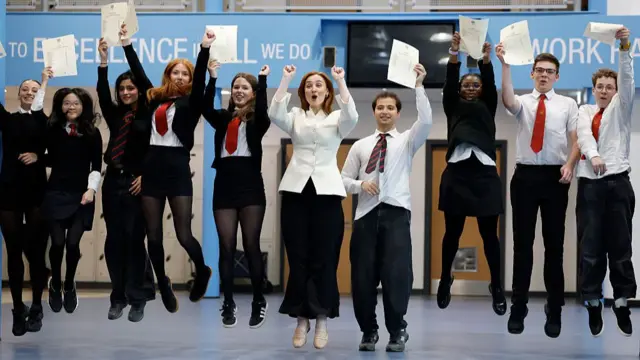 Scotland's education secretary stands in the middle of a line of students jumping in the air holding their exam results.