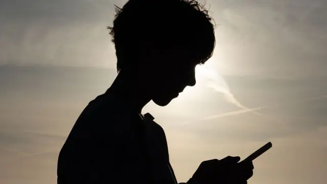 The silhouette of a boy with a smartphone.