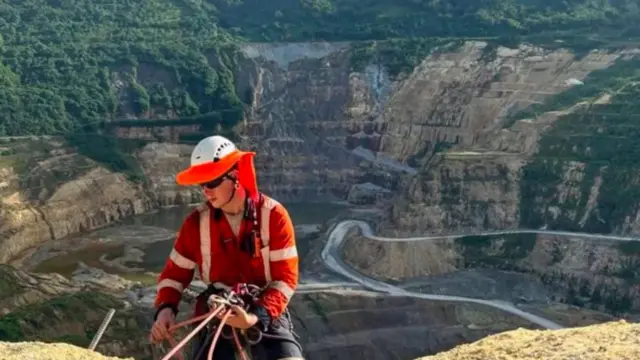 A man attached to a harness over a cliff ledge