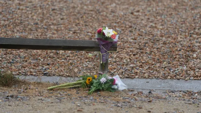 Two bouquets of flowers, laying on the pebbles at the beach, the other tied to a wooden pole, in Shoreham-by-Sea, Sussex.