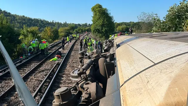 Picture shot from the window of the train showing that it has fallen off the tracks and onto its side while emergency service workers investigate nearby