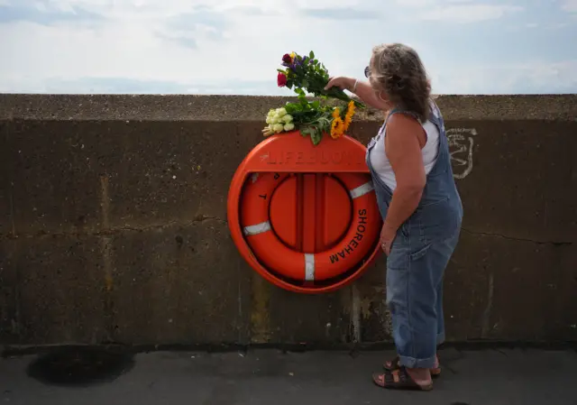 A woman places flowers on a lifebuoy at the beach in Shoreham-by-Sea, West Sussex.