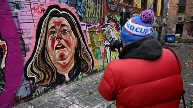 A person takes a photo of a mural of Erin Patterson