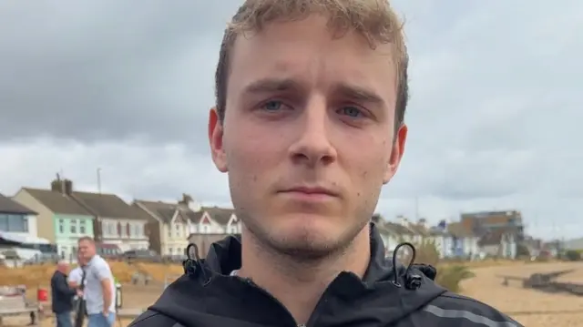 Local resident Toby Venn on Shoreham beach - he has short brown hari and is wearing a black waterproof coat