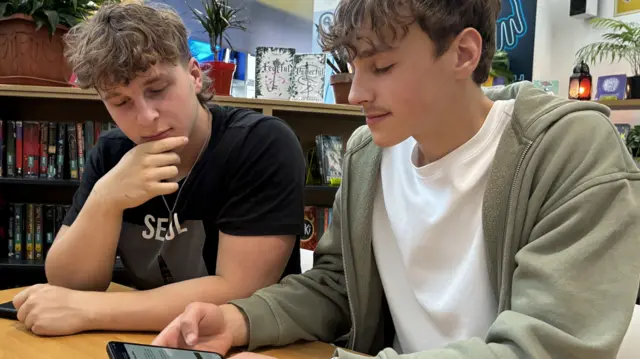 Two young boys look at a phone on which the app is displayed