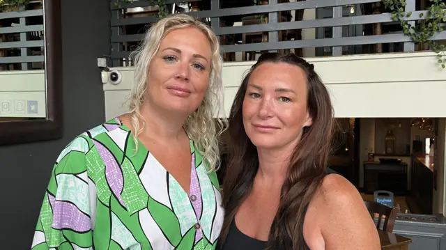 Fiona Stephen and Jen Ashworth. Fiona is wearing a green dress with purple pattern and has blonde hair. Jen has long dark hair and is wearing a black vest.