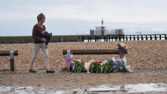 A woman lays flowers on the beach at Shoreham-by-Sea, West Sussex, near the RNLI station. Three members of the same family, including a man, a woman and a teenage girl, have died after getting into trouble in the water off Shoreham-by-Sea, while a younger girl from the same family is in a critical condition, Sussex Police have said. Picture date: Wednesday August 19, 2026.