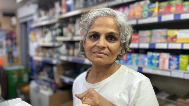 Neha Patel owner of the beach shop stood inside her shop. She has greying hair and is wearing a white shirt.