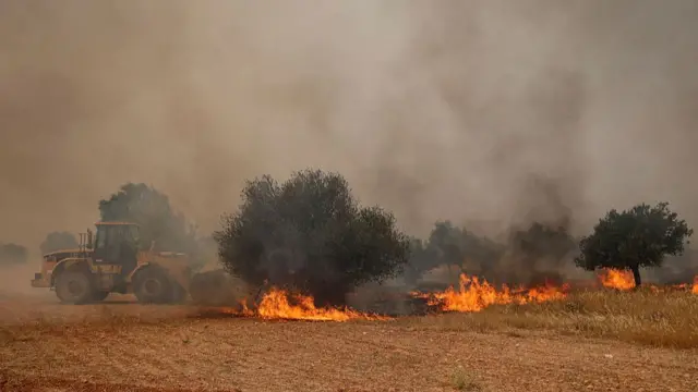Tractor drives through a field trying to put out bush fires with sky filled with smoke