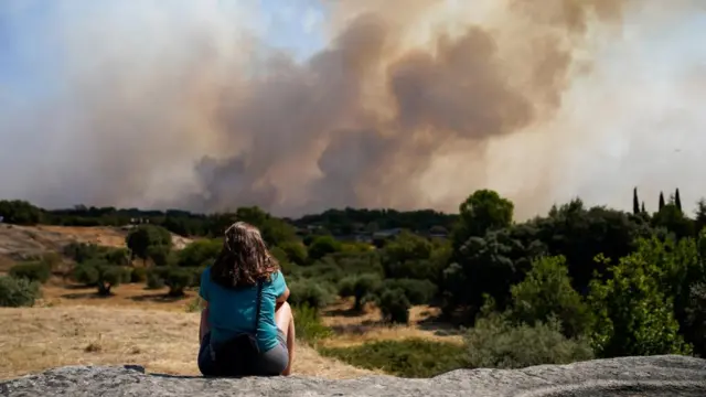 A woman looks on as smoke rises from a wildfire in Madrid last month, 26 July 2026