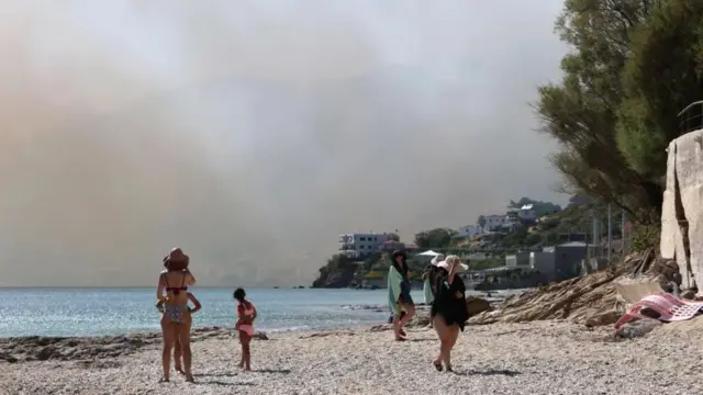 People on a beach in Grete shielding their faces from the sky where lots of smoke is blowing