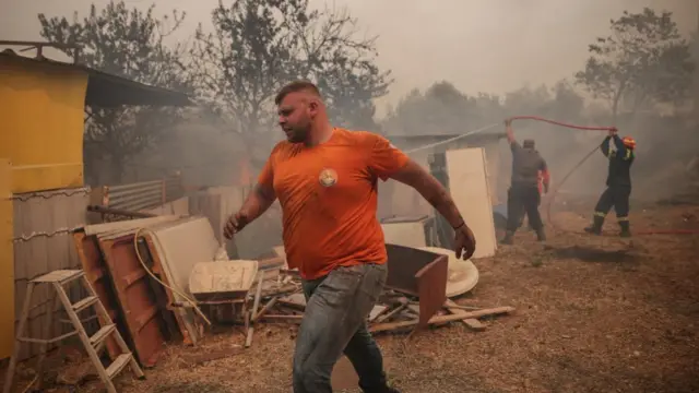 A man runs in the foreground while two others hold a hose in an area affected by fires.