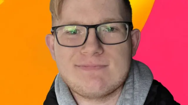 A close-up shot of Alfie with a coloured orange and red background, he is wearing a hoodie and glasses