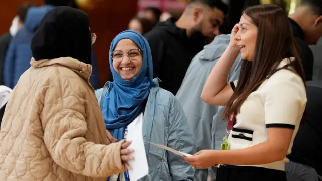 Pupils in a circle smile as they hold results sheets