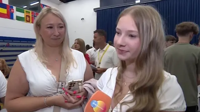 Olivia talks into a BBC microphone, while her mother watches