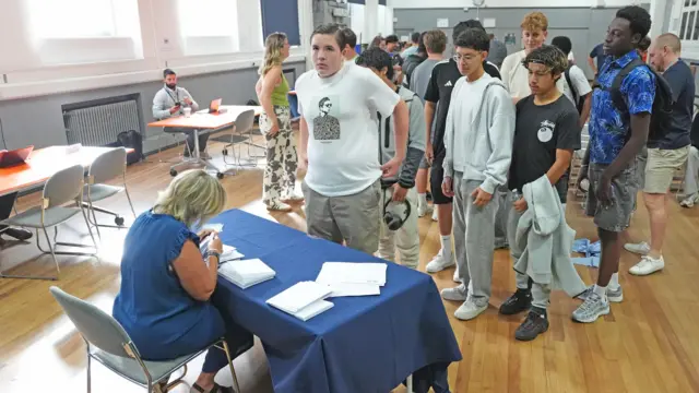 Pupils form a line to collect results envelopes from a teacher