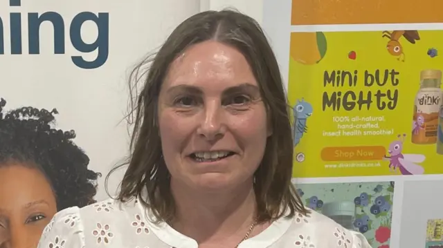 Wynne Hindle smiles into the camera. She wears a white top.