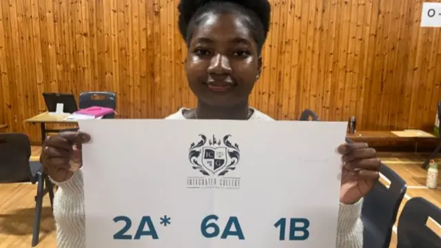 Precious holding her results in a wood panelled room. it lists two A*s, six As and one B