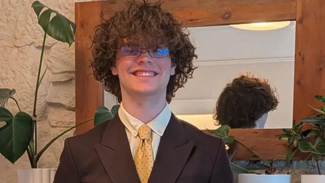 Oscar standing in his living room wearing glasses and a suit, with curly brown hair