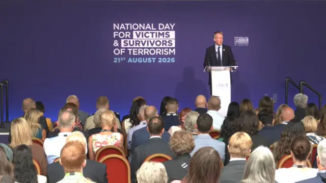 Dan Jarvis is pictured speaking to a room full of people against a purple background