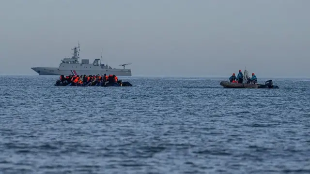 A migrant dinghy sails past a French naval vessel as it sails into the English Channel