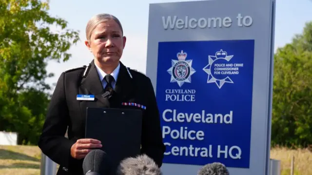 Victoria Fuller is pictured in police uniform speaking behind a bank of microphones.