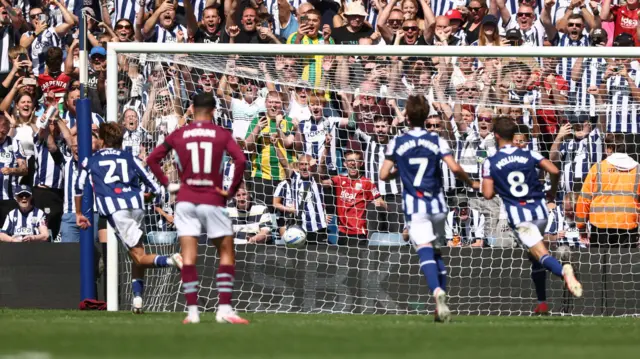 Burnley player stands with hands on hips as West Brom players run in celebration as penalty goes into net