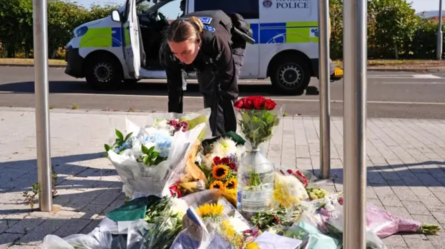A police officer leans down to place two bouquets of flowers at the Cleveland Police HQ Memorial Garden in Middlesbrough