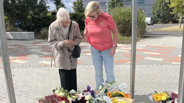 Two woman stand over a memorial comprising several bouquets of flowers at the Cleveland Police HQ memorial garden in Middlesbrough.