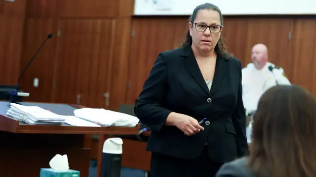 prosecutor, wearing a suit and standing in courtroom facing a witness