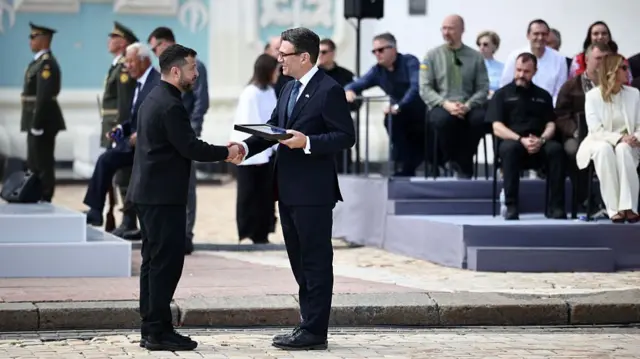 Volodymyr Zelensky shakes Andy Burnham's hand in a ceremony outside a cathedral.