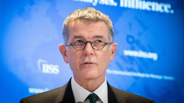 Richard Moore peers over his glasses in front of a blue backdrop