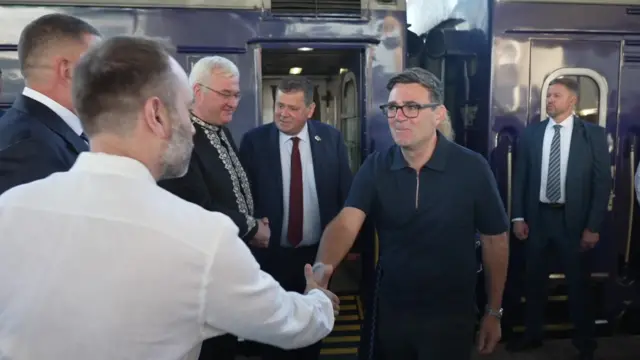 Andy Burnham, stood next to a Ukrainian train, shakes hands with a man in a white shirt.