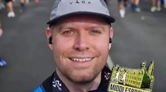 Matthew Blades smiles at the camera while wearing running gear and posing with a running medal