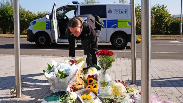 A police officer leaves flowers at the Cleveland Police HQ Memorial Garden in Middlesbrough. A van is visible behind her which says "Cleveland Police".