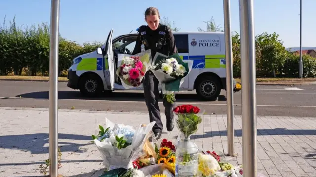 A police officer holds two bouquets of flowers as she walks towards a memorial at the Cleveland Police HQ Memorial Garden in Middlesbrough