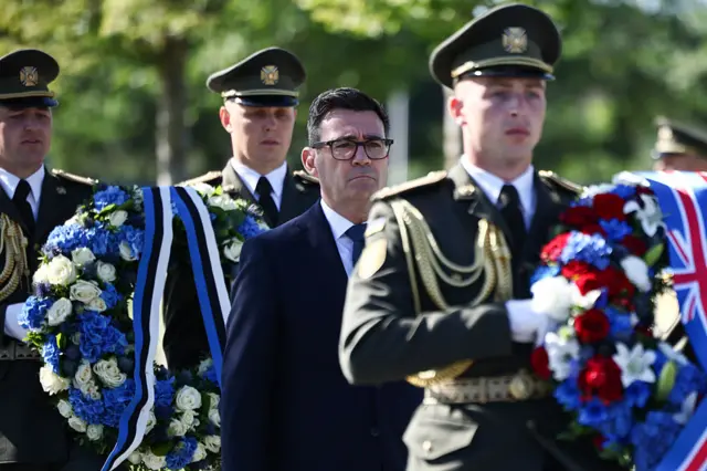 Andy Burnham standing between Ukrainian soldiers carrying wreathes.