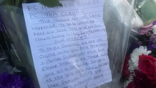 A piece of paper tucked inside the plastic wrapping a bouquet of flowers. It reads: "PC Matthew Blades. PC Tom Clough. This should never have happened. To go to work to keep our area safe and to not return home is truly heart breaking. Our heroes. To their families, we are all crying with you. As a stranger I cannot fathom your pain but please know we are stood with you as a community. Sending all the love in the world to both their families, friends and colleagues."
