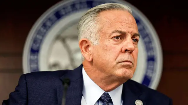 A white man with short hair wearing a blue suit, white shirt and blue tie.