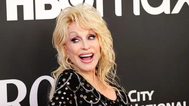 Dolly Parton wears a black shirt and has blonde hair