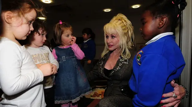 Dolly Parton bending down to talk with several toddlers
